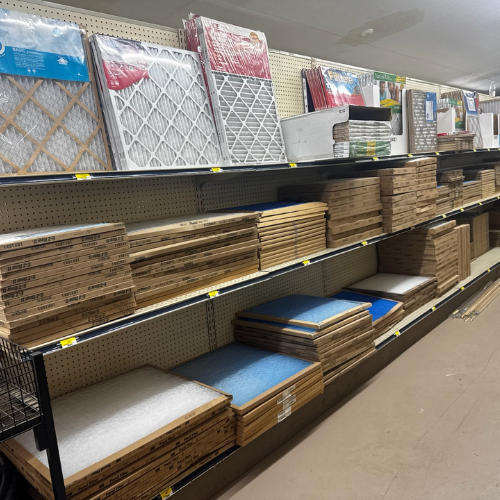Store aisle with wooden shelves stacked with air filters in various sizes, colors, and packaging. Clean, organized setting, suggesting a hardware store environment.