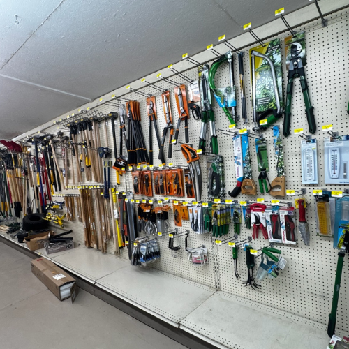 A hardware store aisle displays various gardening tools like rakes, shears, and pruners hanging on a pegboard wall, conveying an organized and practical atmosphere.