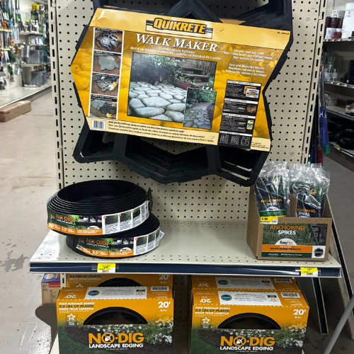 Store display with Quikrete Walk Maker, No-Dig landscape edging, and anchoring spikes. Products set on shelves suggest a DIY garden theme.