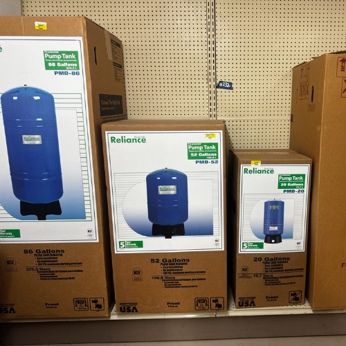 Boxes of Reliance pump tanks in a store, displaying models PMD-86, PMD-52, and PMD-20. Each box shows a blue tank image, labeled with gallon size.