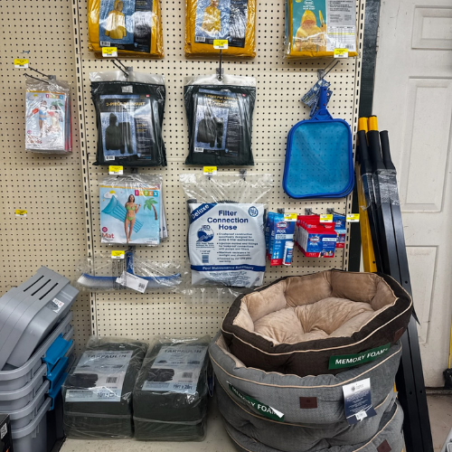 Store shelf display with pet supplies. Items include memory foam pet beds, pool hoses, filters, and cleaning tools, portraying a practical, organized setting.