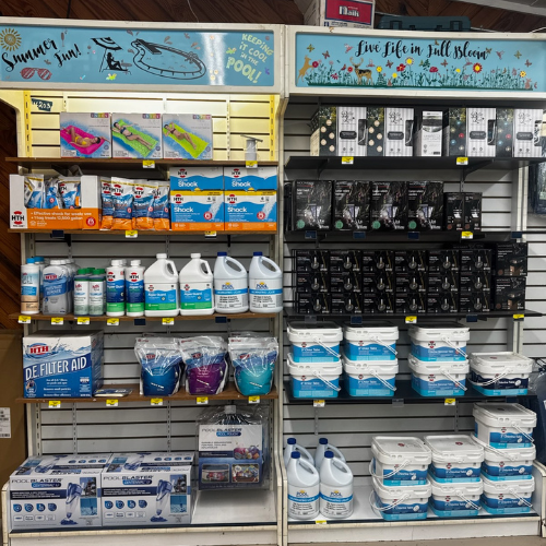 Store shelves display pool maintenance products and cleaning supplies with colorful banners above reading 