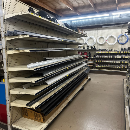 Shelves of a hardware store displaying metal strips and piping. Rings of coiled pipes are visible on the wall. The space is organized and industrial.