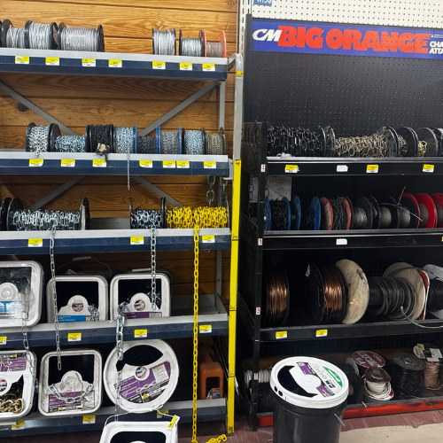 Shelves with various spools of wire and chain, labeled and organized by type. Display signage reads 