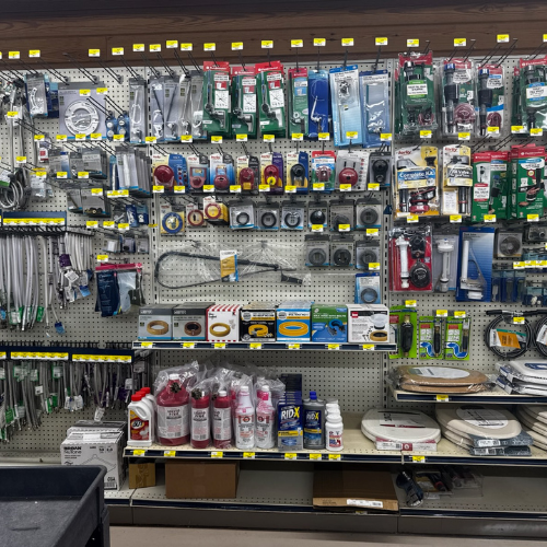 A hardware store display shows neatly organized plumbing supplies including hoses, fittings, sealants, and tools. The shelves are well-stocked and labeled.