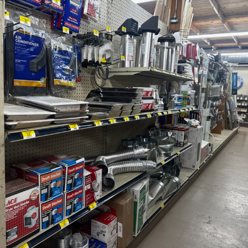 Hardware store aisle with neatly organized air conditioner filters, vent pipes, and draft blockers on shelves. Industrial, practical atmosphere.