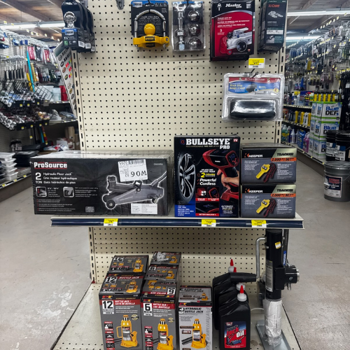 Hardware store display featuring automotive tools and accessories. Shelves hold wrenches, a jack, air compressors, and repair kits, creating a practical and organized atmosphere.