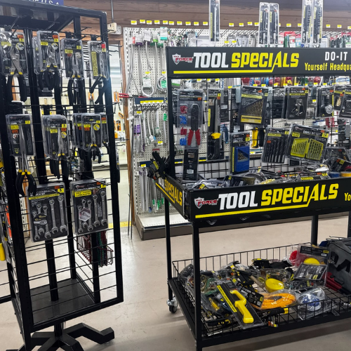 A hardware store aisle showcasing a variety of tools on racks. Signs reading 