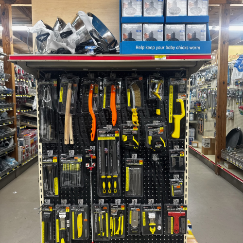 A store display featuring various tools like saws and brushes in bright yellow packaging on a pegboard. A sign above reads, 