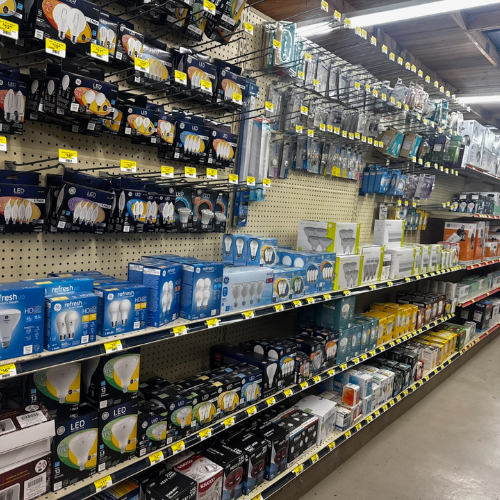 Store aisle with shelves displaying a variety of LED light bulbs and electrical items in colorful packaging. The setting is organized and well-lit.