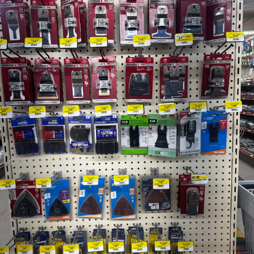 A display of various saw blades and accessories in a store, arranged on a pegboard. Each item is in packaging with bright yellow price tags.