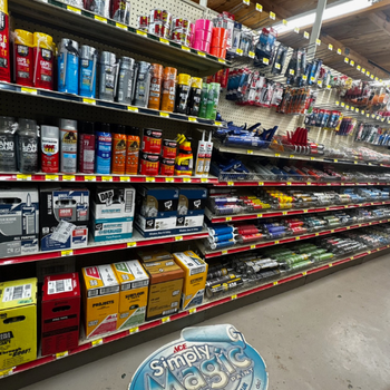 Hardware store aisle with colorful spray paints, adhesives, and tools neatly organized on shelves. Bright lighting and a clean, orderly appearance.
