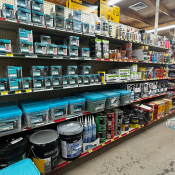 A well-organized hardware store aisle with shelves stocked with nails, screws, glues, and paint supplies. The image conveys a neat, functional atmosphere.
