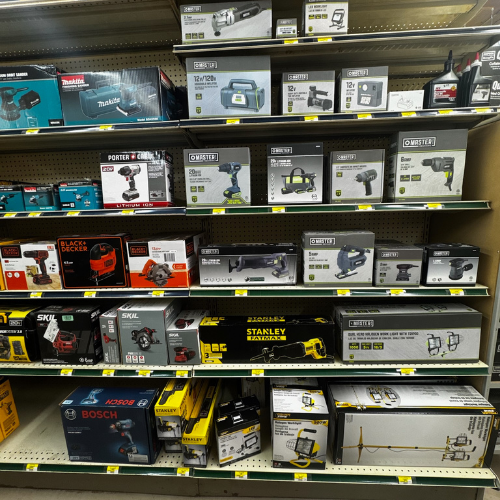 A store shelf filled with boxed power tools, including drills and saws from brands like Makita and Stanley. The display is organized and brightly lit.