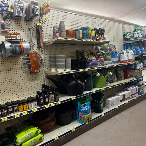 A store aisle with gardening supplies, featuring pots, soil, watering cans, and plant food on shelves. Bright, organized, with earth-tone colors.