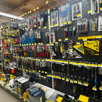 A well-organized hardware store aisle displays various hanging tools, including screwdrivers and pliers, on a black metal wall with yellow labels.