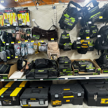 Display of various tool bags and boxes on metal shelves in a store. Products include brands like AWP and Dewalt, with black and green packaging.