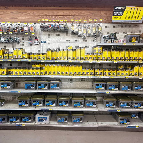 A hardware store shelf displays a variety of tools and accessories. Bright yellow packaging and blue storage cases create an organized, industrial look.