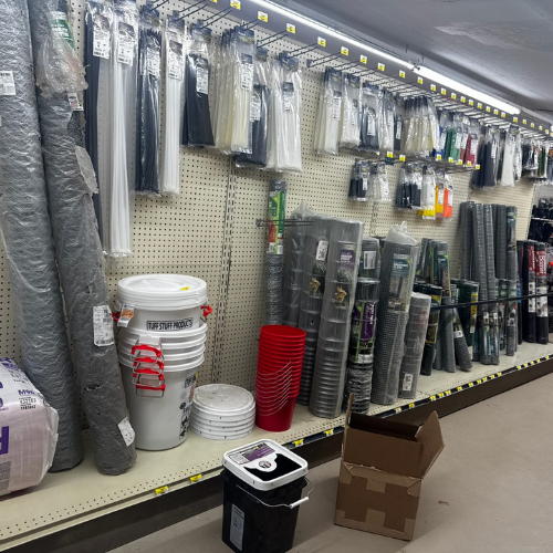 Shelves stocked with hardware supplies, including rolls of mesh, buckets, and pipes, convey a utilitarian and organized retail environment.